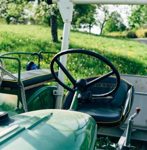 Close-up of a classic green tractor with blooming trees in the background.