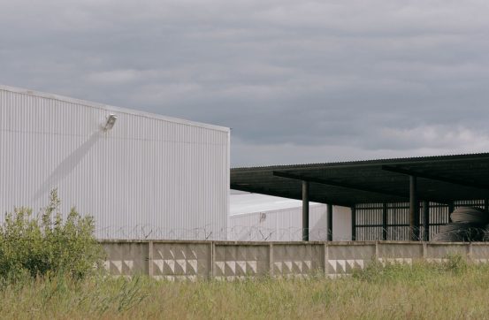 White industrial building backdrop against a grass field and overcast sky.